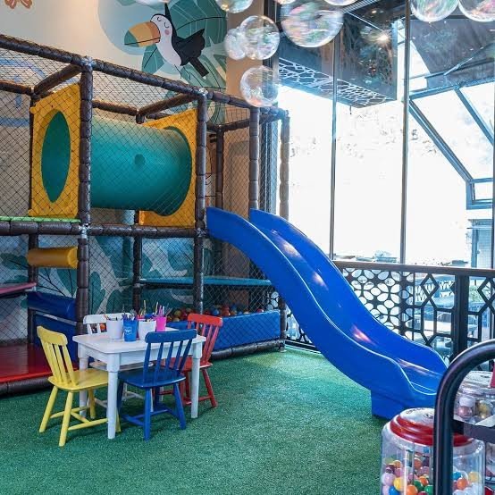 Playground indoor com escorregador azul e mesinhas infantis